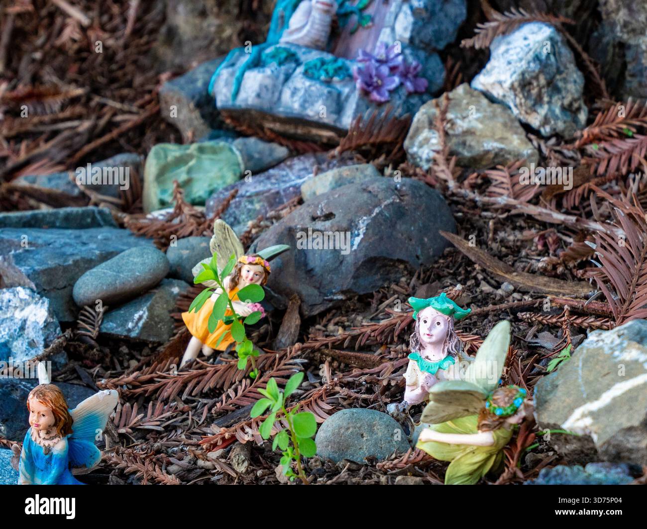 Piccole statuette fiabesche incastonate tra rocce e aghi di sequoia in un giardino in miniatura stravagante. Foto Stock