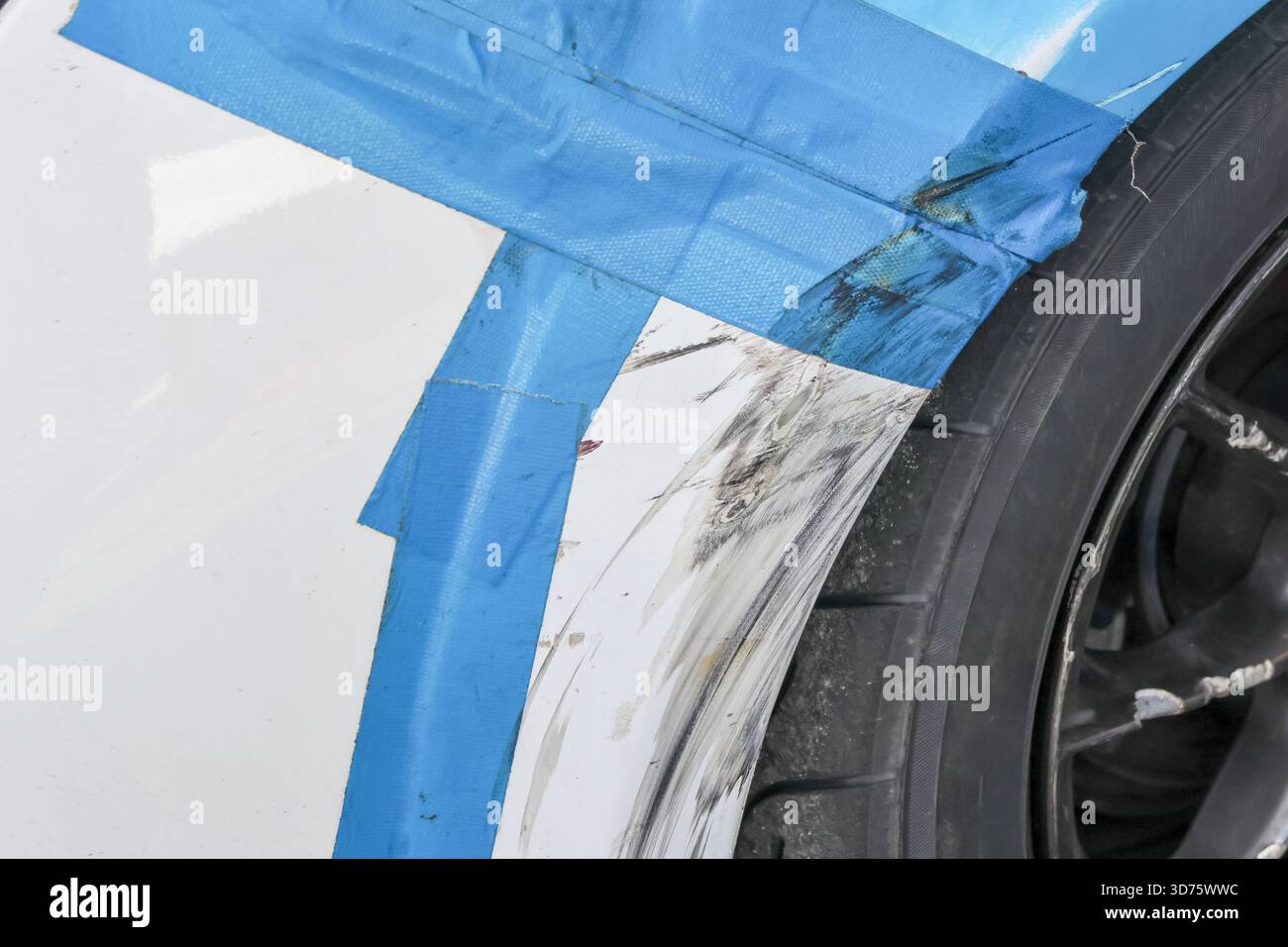 Primo piano dei danni alla vettura con graffi profondi sul parafango bianco. Il nastro di mascheratura blu protegge il pannello del veicolo durante la riparazione della carrozzeria e i lavori di verniciatura da parte di professionisti Foto Stock