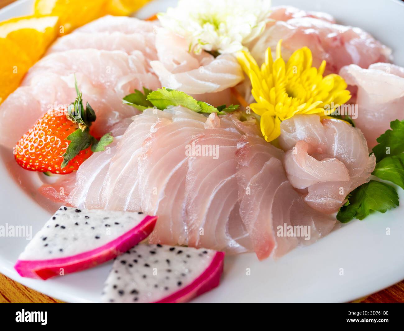 Sashimi di pesce thailandese fresco servito con frutta tropicale e fiori commestibili su piatto bianco, che rappresenta una sana cucina giapponese, una cucina pulita e fusion Foto Stock
