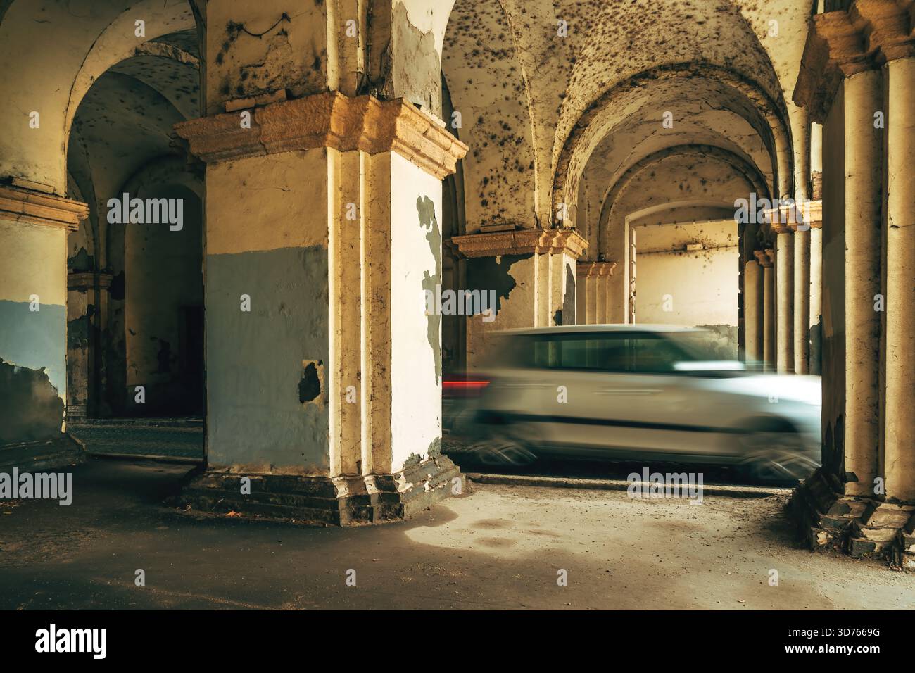 Le auto in movimento si sfocano passando attraverso un vecchio corridoio arcuato in decadenza con pareti sbucciate e una luce spettacolare, mescolando il movimento urbano con l'arco storico Foto Stock