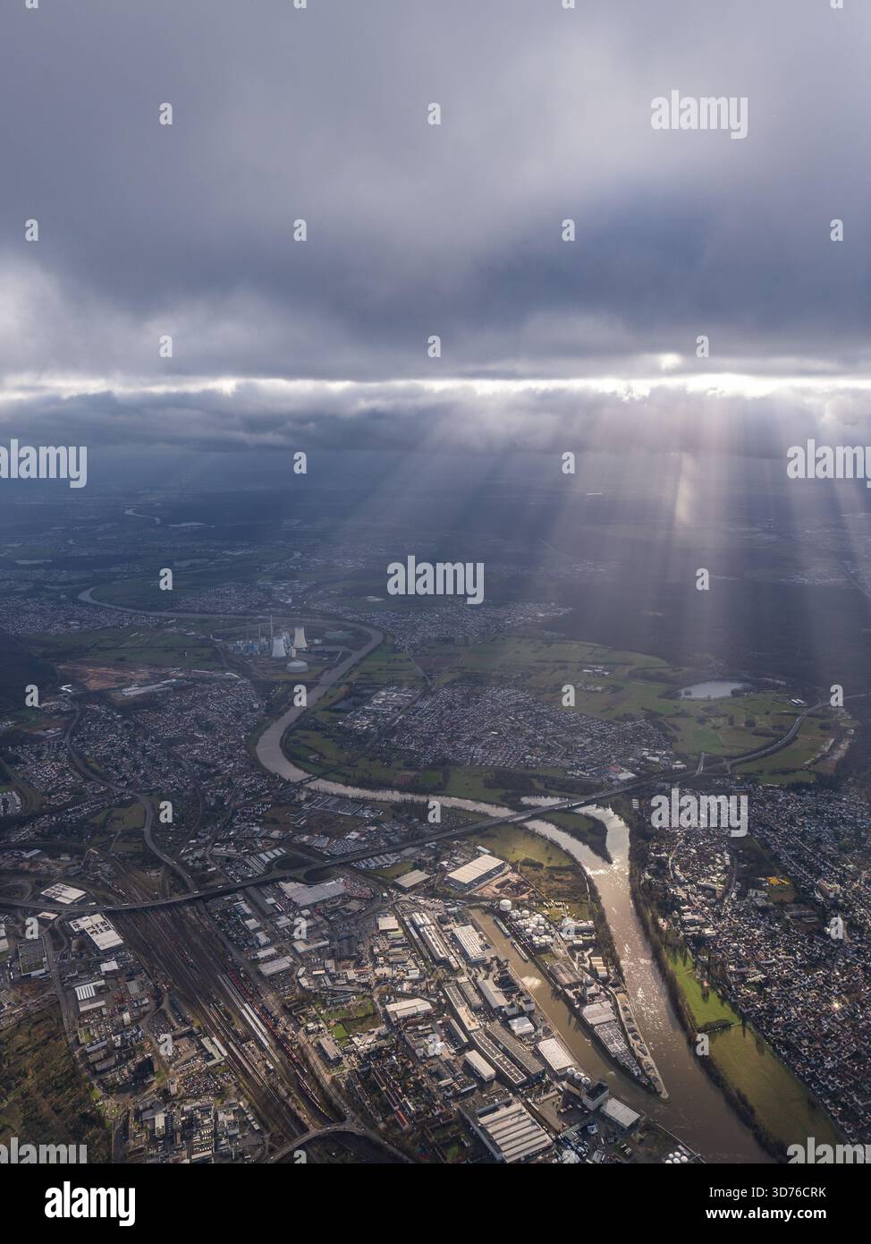 Spettacolare vista aerea di una città industriale e di un fiume tortuoso, con potenti raggi crepuscolari del sole (raggi di Dio) che si infrangono attraverso nuvole di tempesta buie Foto Stock