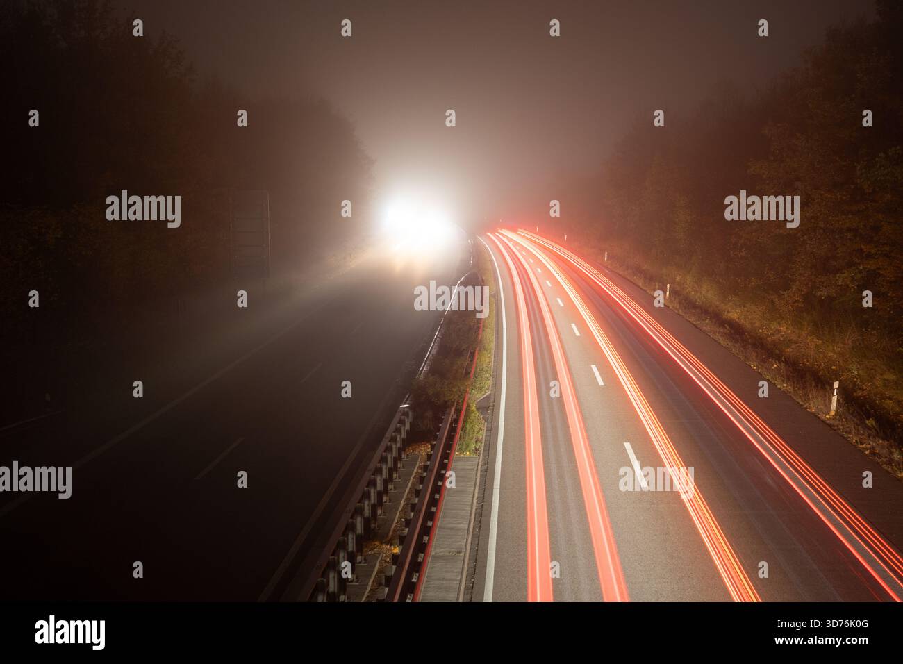 Scatti notturni ad alta esposizione di un'autostrada, dove i fari bianchi luminosi e le tracce di luce rossa svaniscono rapidamente in una densa tasca di Foto Stock
