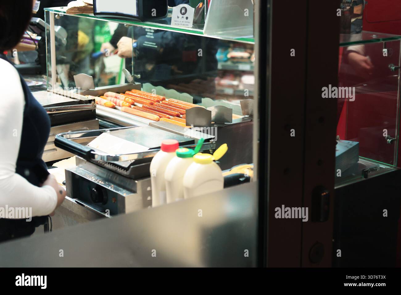 Un venditore di cibo di strada che prepara hot dog, mostra salsicce rosse brillanti su un grill, salse e un cliente che aspetta nelle vicinanze. Foto di alta qualità Foto Stock