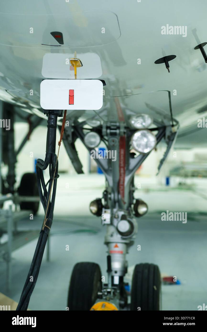 Vista dettagliata del sistema di carrello di atterraggio dell'aeromobile, che mostra i componenti tecnici e i fili durante un controllo di manutenzione in un hangar alla luce del giorno. Foto Stock