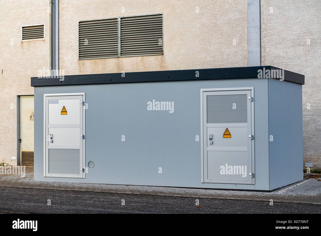 Un edificio grigio di attrezzature si trova in un'area urbana. È dotato di cartelli di avvertenza ed è realizzato con materiali robusti. Le infrastrutture nelle vicinanze completano l'offerta Foto Stock