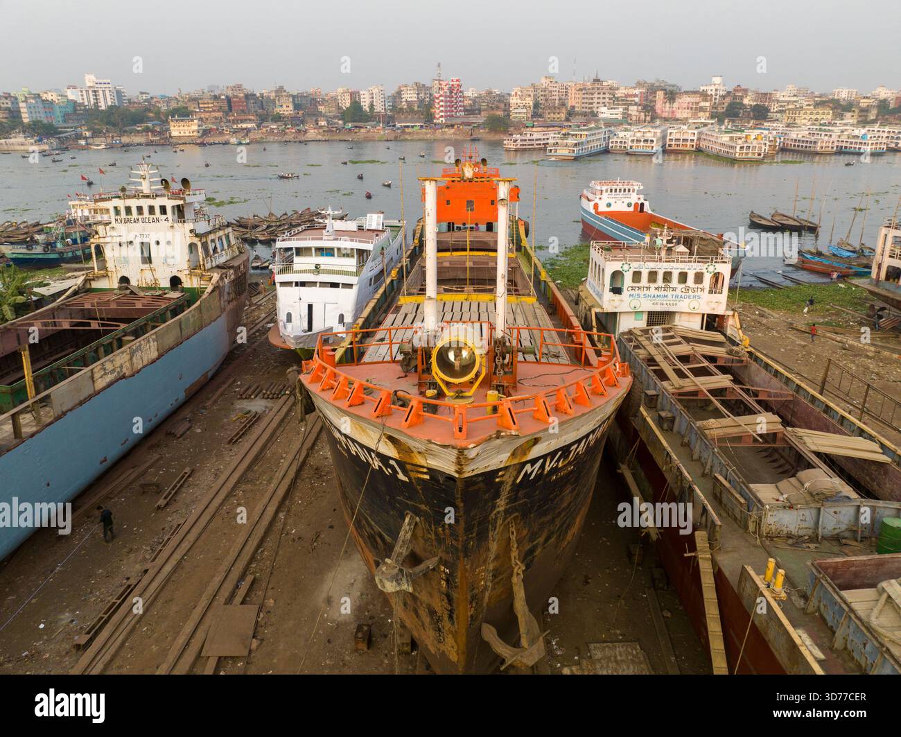 Vista aerea delle colossali navi attraccate nel porto, i loro scafi intemprati testimoniano il tempo, sullo sfondo dello skyline urbano di Dacca, Dacca, DHA Foto Stock
