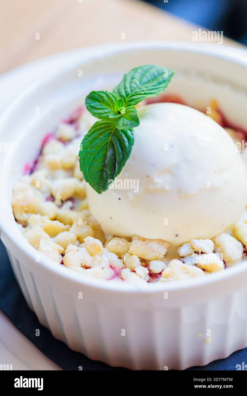Delizioso dessert servito in un ramekin bianco con menta fresca e cremoso gelato alla vaniglia su un croccante fruttato Foto Stock