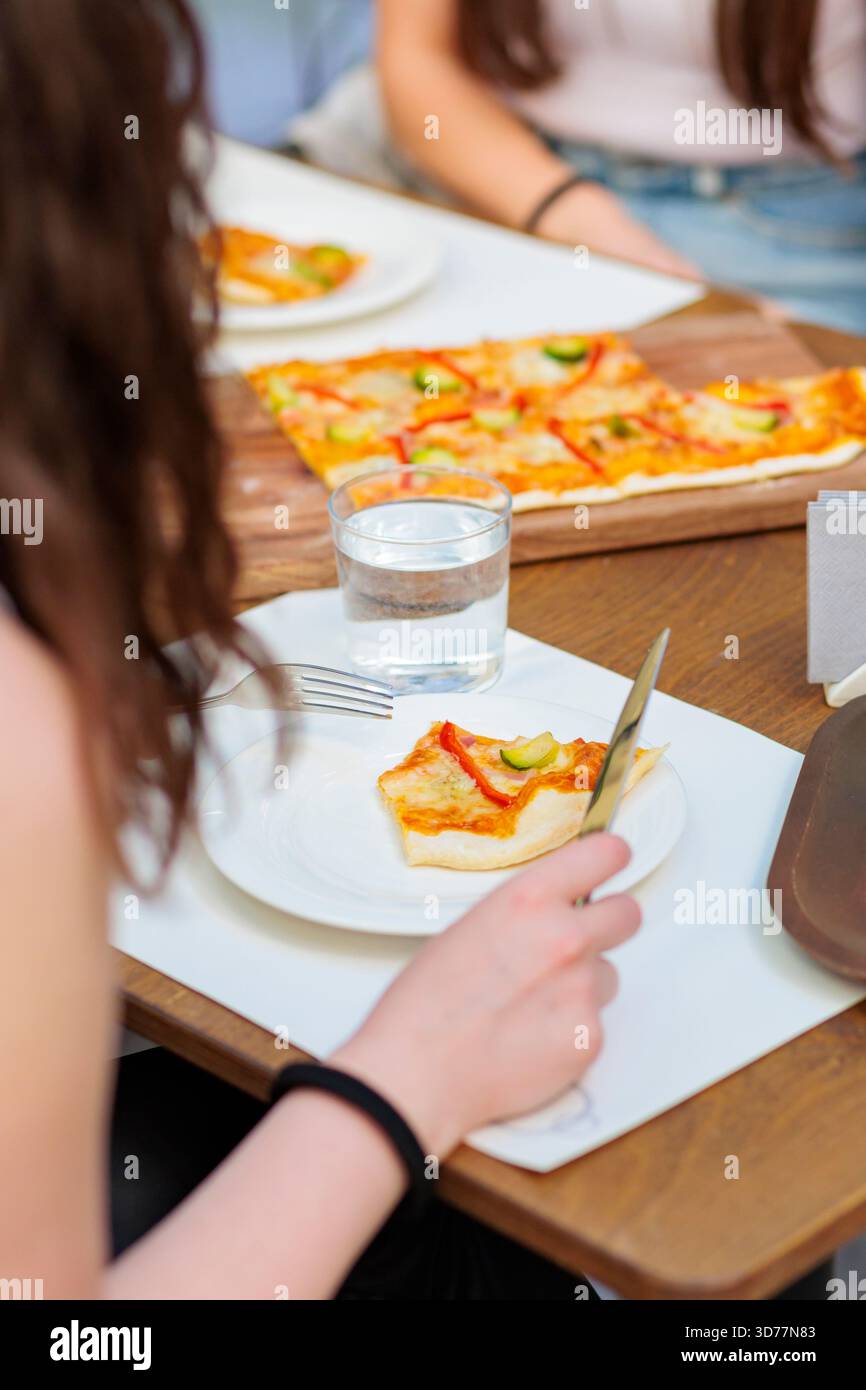 durante l'ora di pranzo, la persona può gustare una fetta di pizza con verdure in un accogliente tavolo del ristorante Foto Stock