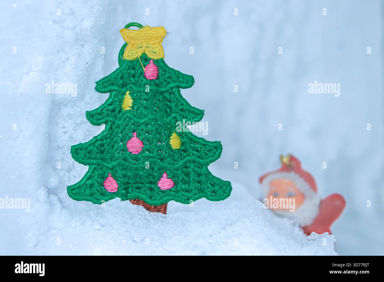 Scenario invernale orizzontale con un albero di Natale ricamato sulla neve glaciale e un Babbo Natale sfocato dietro di esso, creando un divertente Micro World festivo. Foto Stock