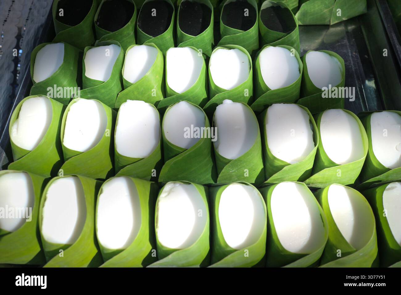 Autentica gelatina tailandese di latte di cocco, in tazze di foglie di banana, con texture cremose a contrasto con avvolgimento verde naturale per un tema dessert sostenibile. Foto Stock