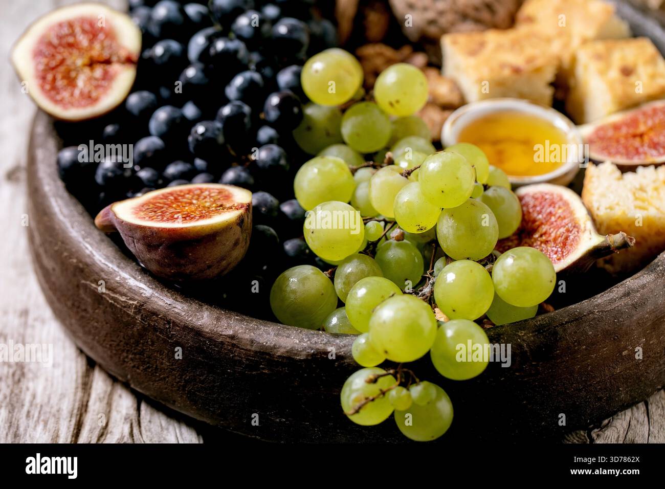 Antipasti di vino con diverse uve, fichi, noci, pane, miele e formaggio di capra su piatto di ceramica su vecchio sfondo di legno. Primo piano Foto Stock