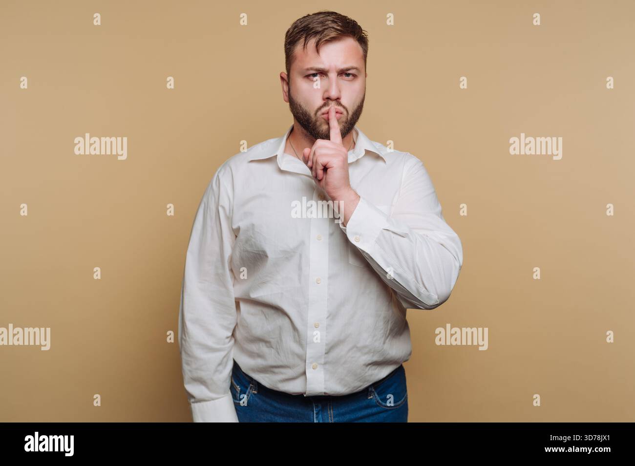 ritratto di un giovane che tiene un dito sulle labbra, segnalando il silenzio, incarna mistero e segretezza su sfondo beige Foto Stock