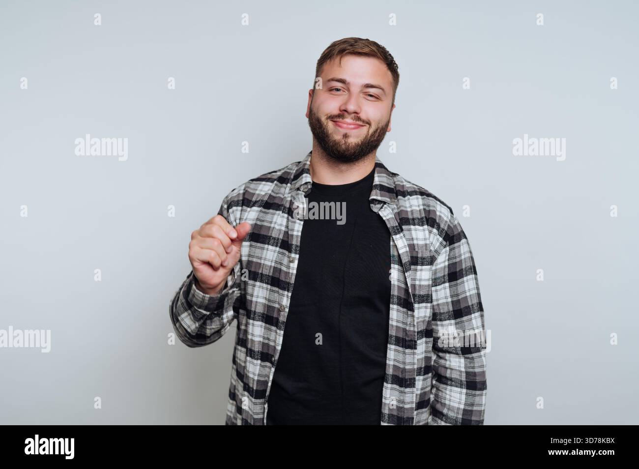 il ritratto di un giovane uomo si erge con sicurezza con un sorriso sottile e un gesto, ritraendo intrighi su sfondo bianco Foto Stock