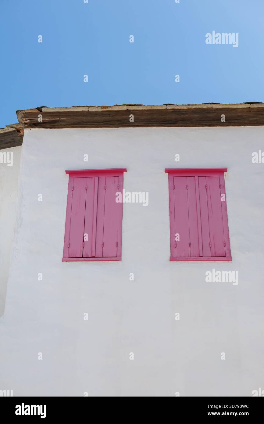 edificio bianco con persiane di legno rosa contro un cielo blu Foto Stock