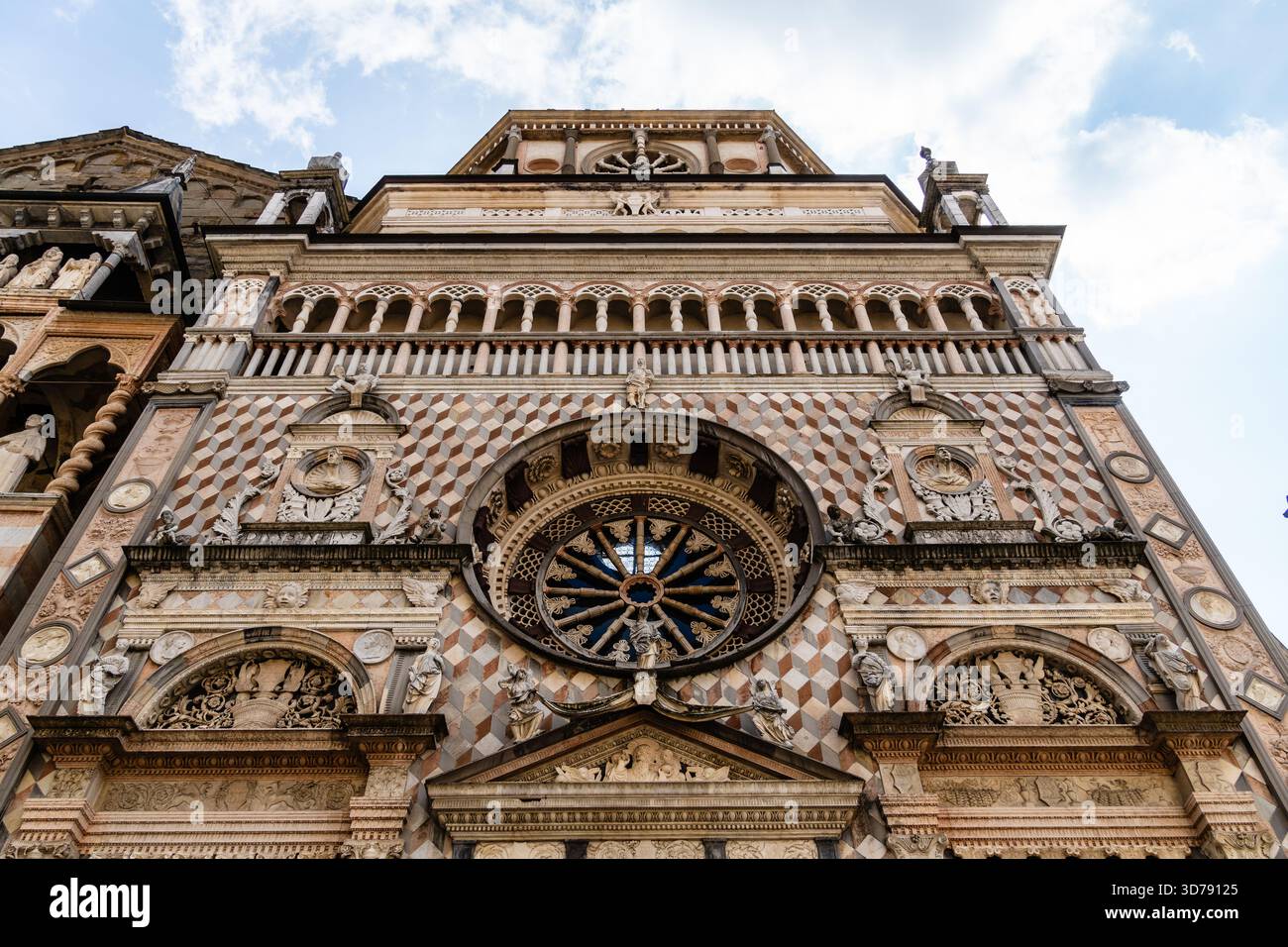 Una prospettiva verso l'alto cattura la facciata ornata della Capella Colleoni, una cappella rinascimentale di Bergamo, sotto un cielo parzialmente nuvoloso. Foto Stock