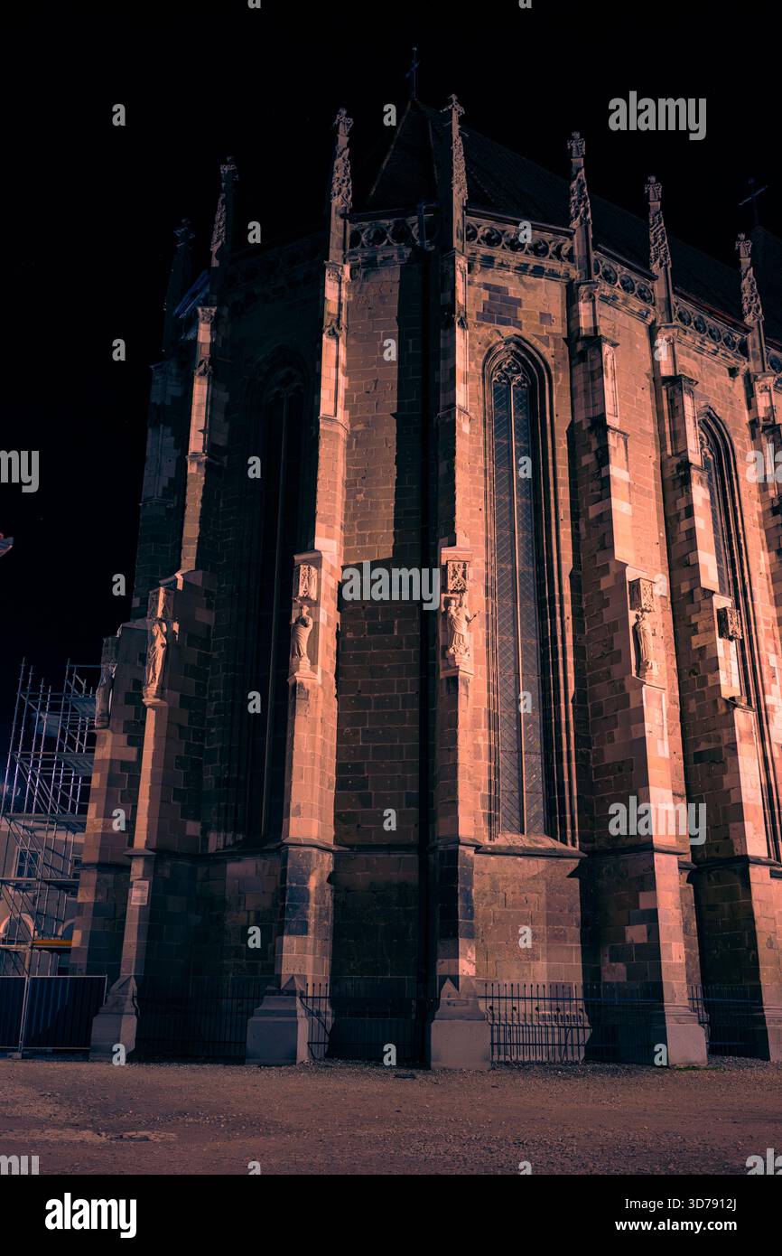 Drammatico ritratto notturno della Chiesa Nera (Biserica Neagră) a Brașov, Romania. Le pareti di pietra scura sono evidenziate da un'illuminazione calda e suggestiva. Foto Stock