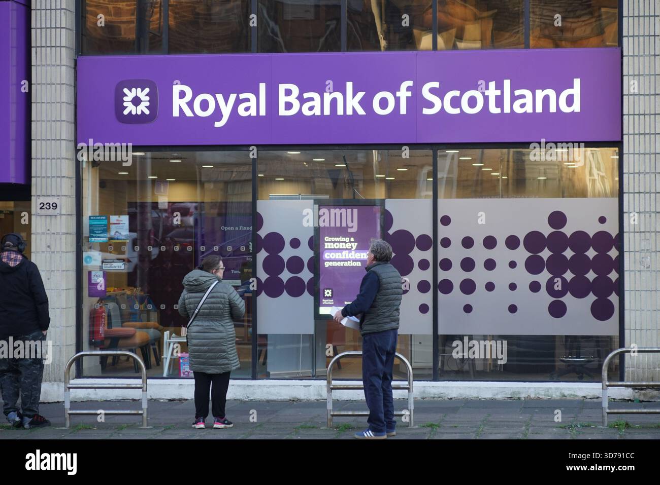 Persone che si trovano fuori da una filiale della Royal Bank of Scotland in una strada cittadina, catturate durante una tipica giornata invernale in Scozia. Edimburgo, Scozia Foto Stock