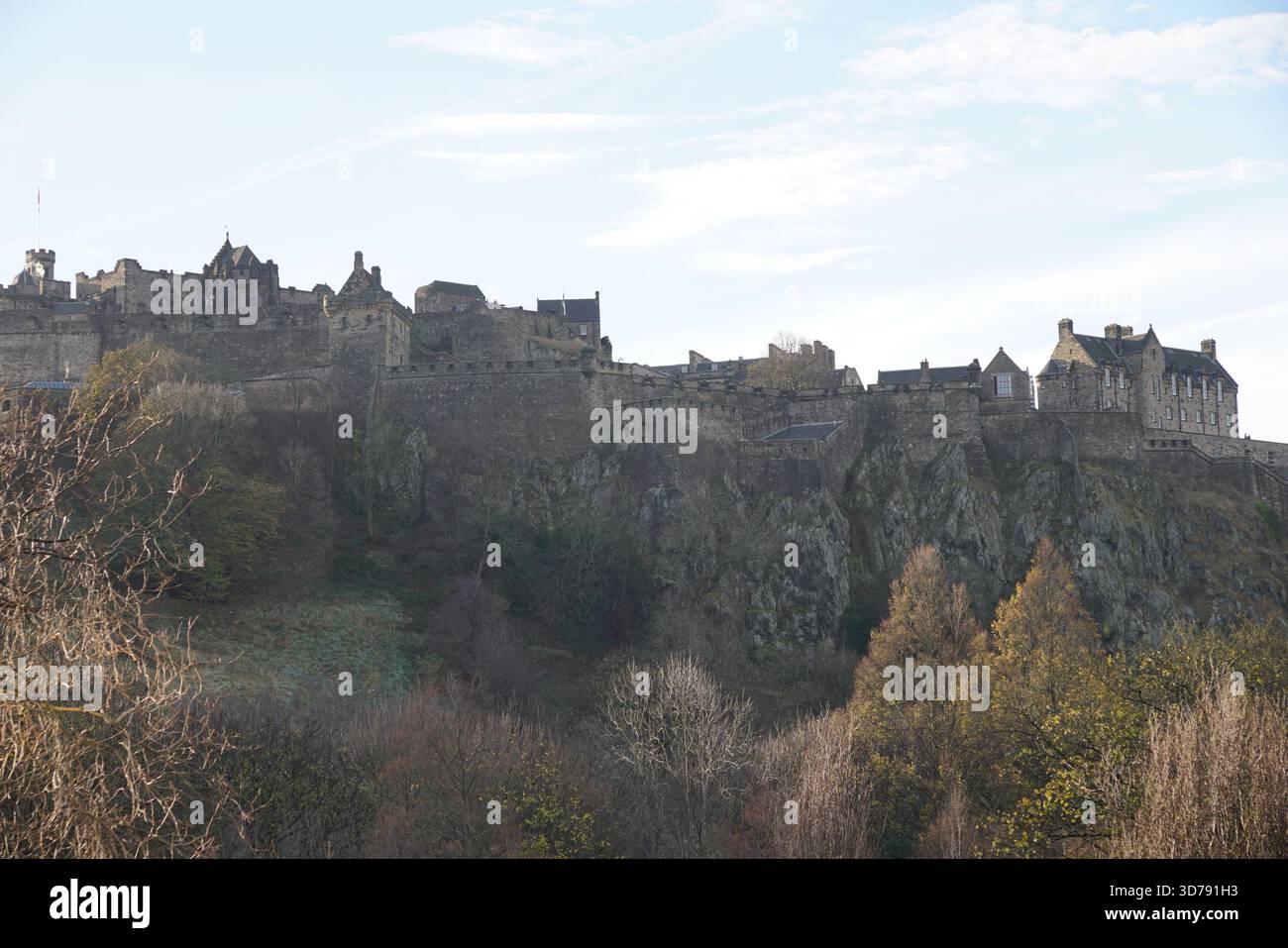 Vista del Castello di Edimburgo sulla sua collina rocciosa, che si innalza sopra gli alberi autunnali sotto un cielo limpido. Edimburgo, Scozia Foto Stock