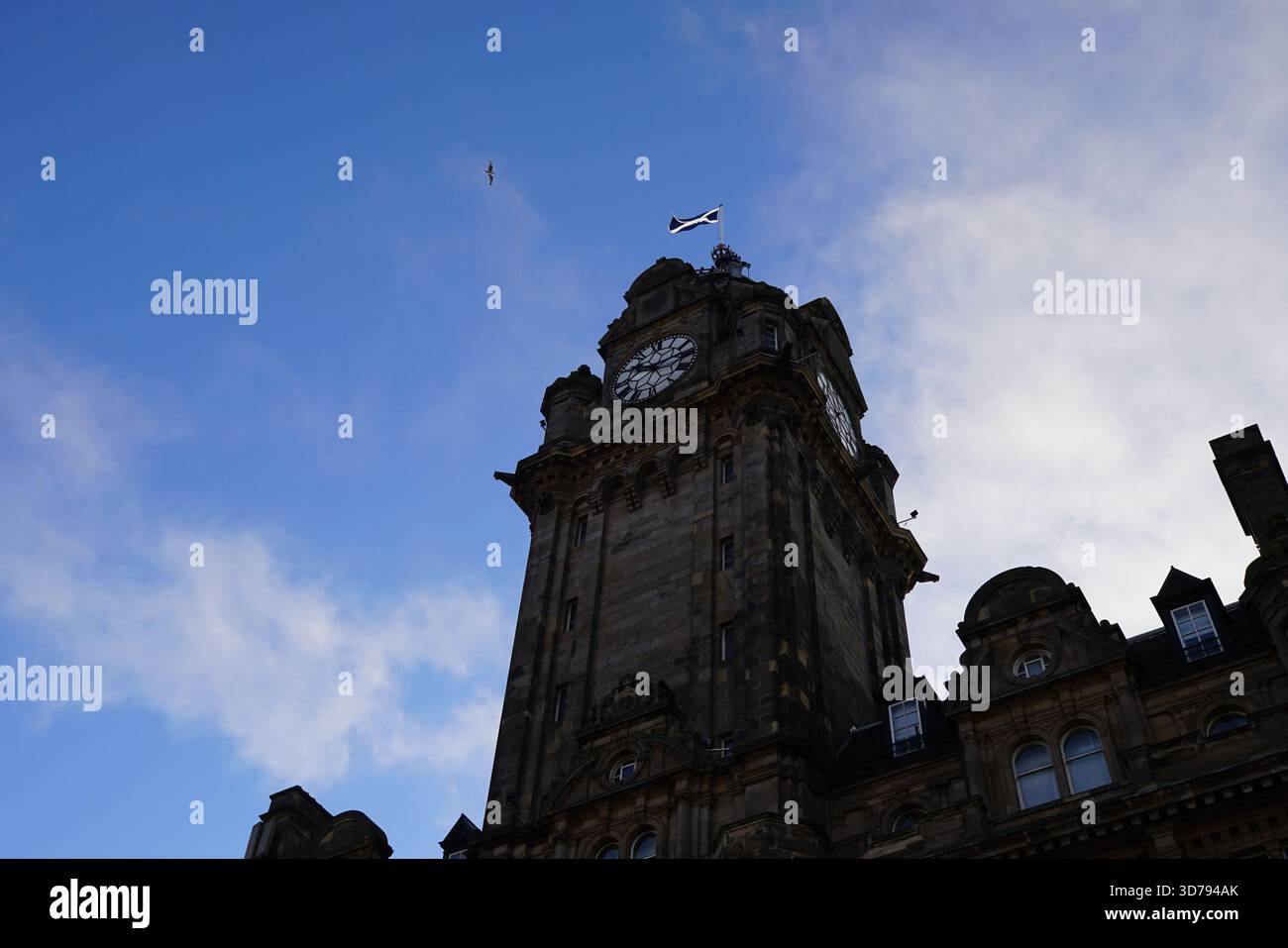 La torre dell'orologio del Balmoral Hotel a Edimburgo si staglia contro un cielo blu con la bandiera scozzese che sventola sopra. Edimburgo, Scozia Foto Stock