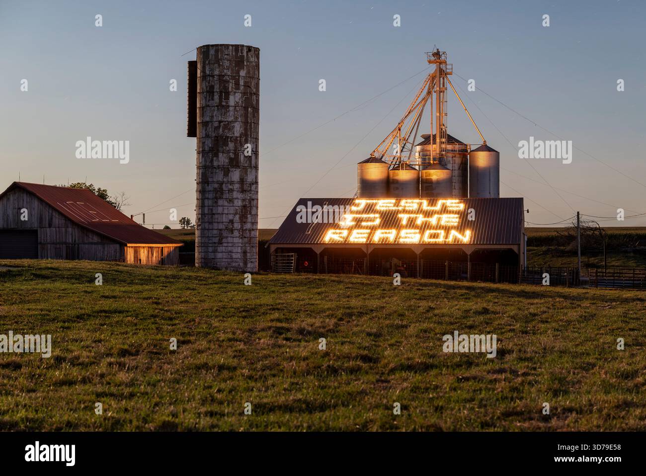 Shields Farm lungo la US 40, Putnam County, Indiana, presenta architettura in mattoni degli anni '1840, fienili e silos, con messaggi religiosi illuminati a LED al tramonto. Foto Stock