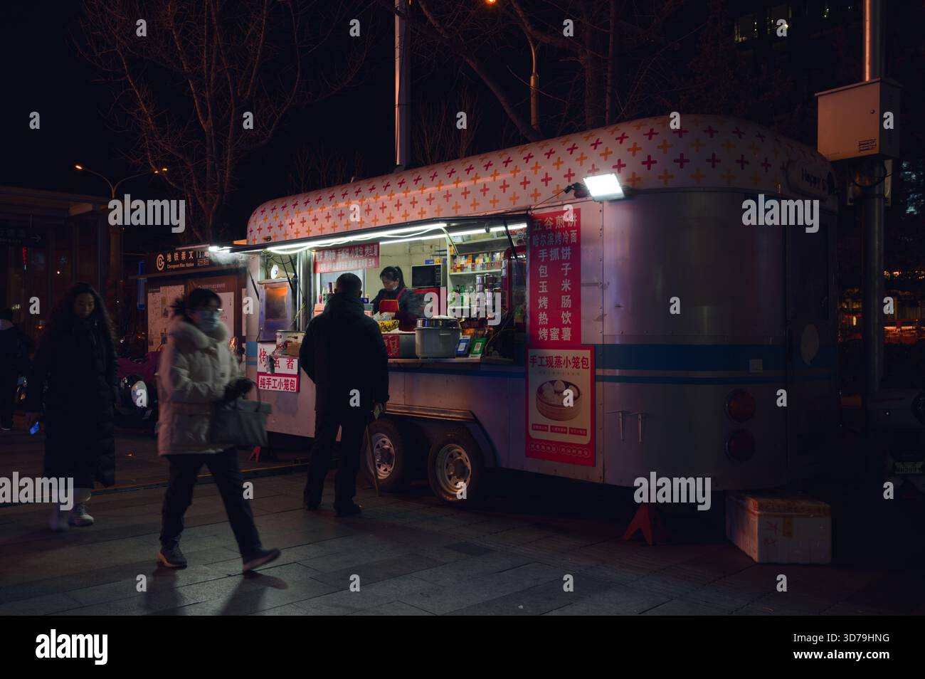 Il trailer del cibo di strada a tarda notte si illumina durante l'inverno di Pechino, mentre i pedoni si affrettano a passare Foto Stock