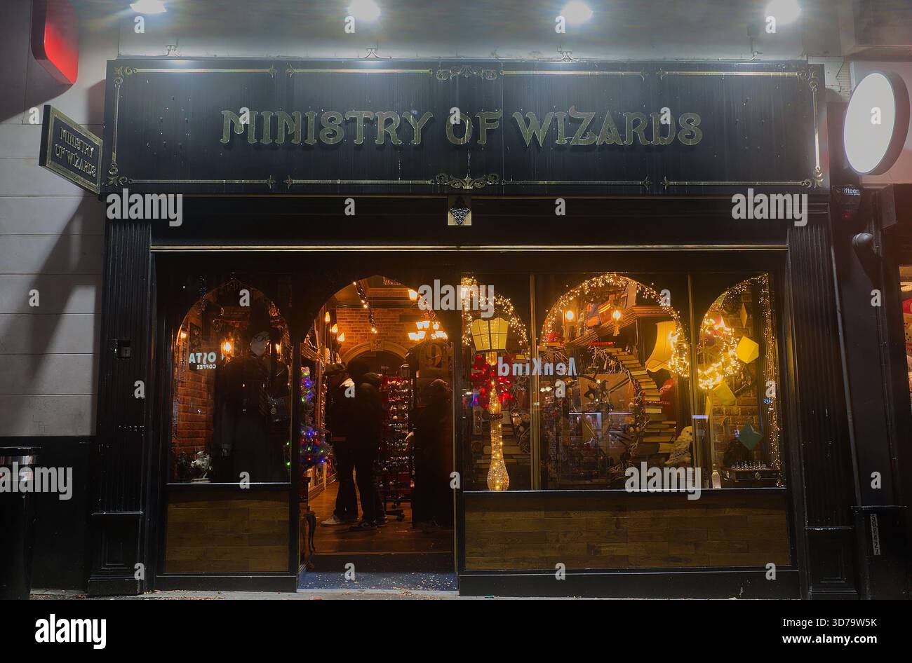 Il negozio a tema magico del Ministero dei Maghi a Lord St, Liverpool, di notte. La facciata scura e in vecchio stile e le finestre brillano di calde luci dorate. Foto Stock