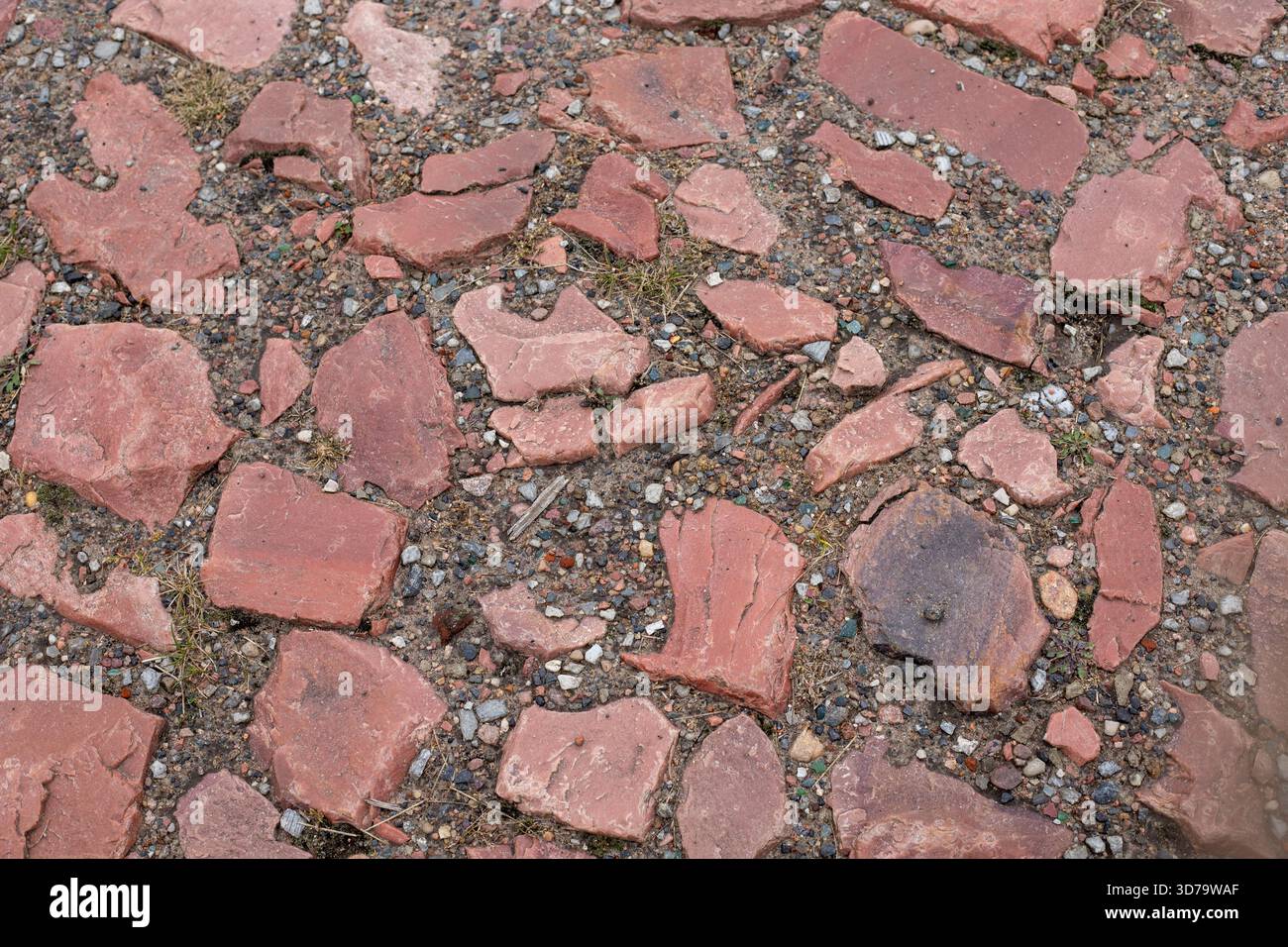 Vecchi ciottoli rossi, antichi marciapiedi con pietre marroni irregolari. Antica pavimentazione di mattoni acciottolati con grandi pietre. Foto Stock
