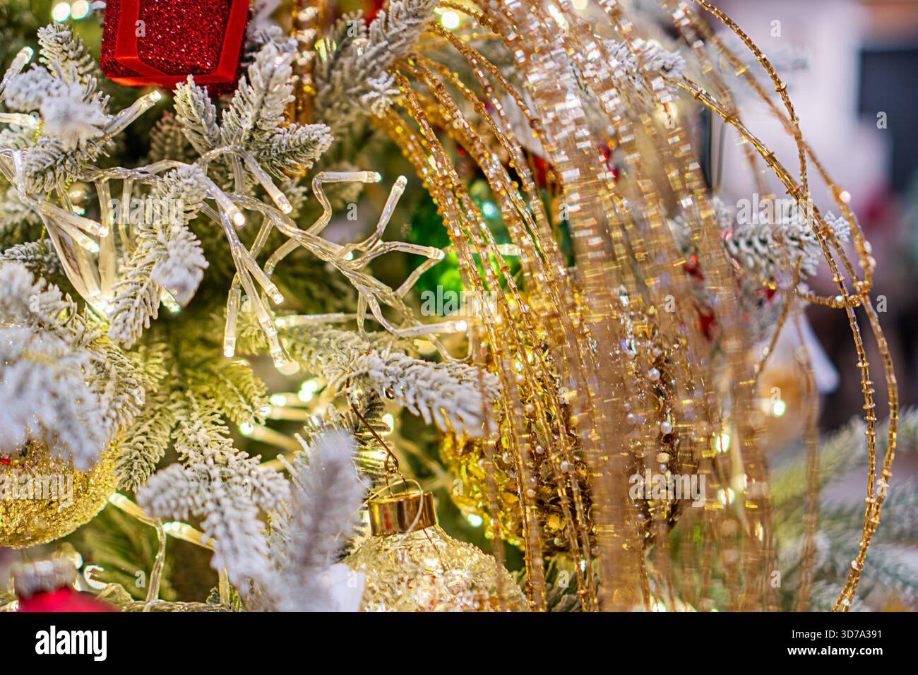 Un albero di Natale decorato sia per Capodanno che per Natale, caratterizzato da un mix di ornamenti bianchi, argentati, rossi e verdi, illuminati da perline dorate Foto Stock