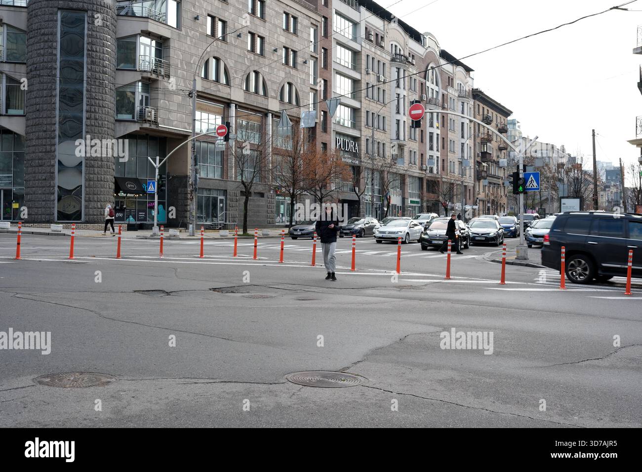 I pedoni attraversano un trafficato incrocio cittadino pieno di auto e negozi intorno. 24 novembre 2025 Kiev, Ucraina Foto Stock