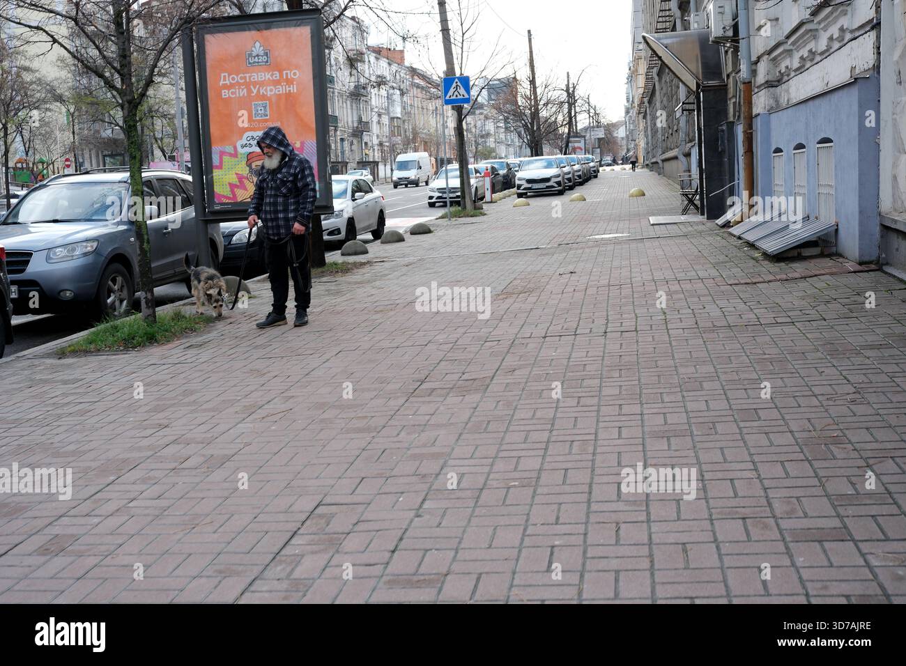 Un uomo sta con il suo cane in una strada tranquilla, circondato da auto parcheggiate. 24 novembre 2025 Kiev, Ucraina Foto Stock