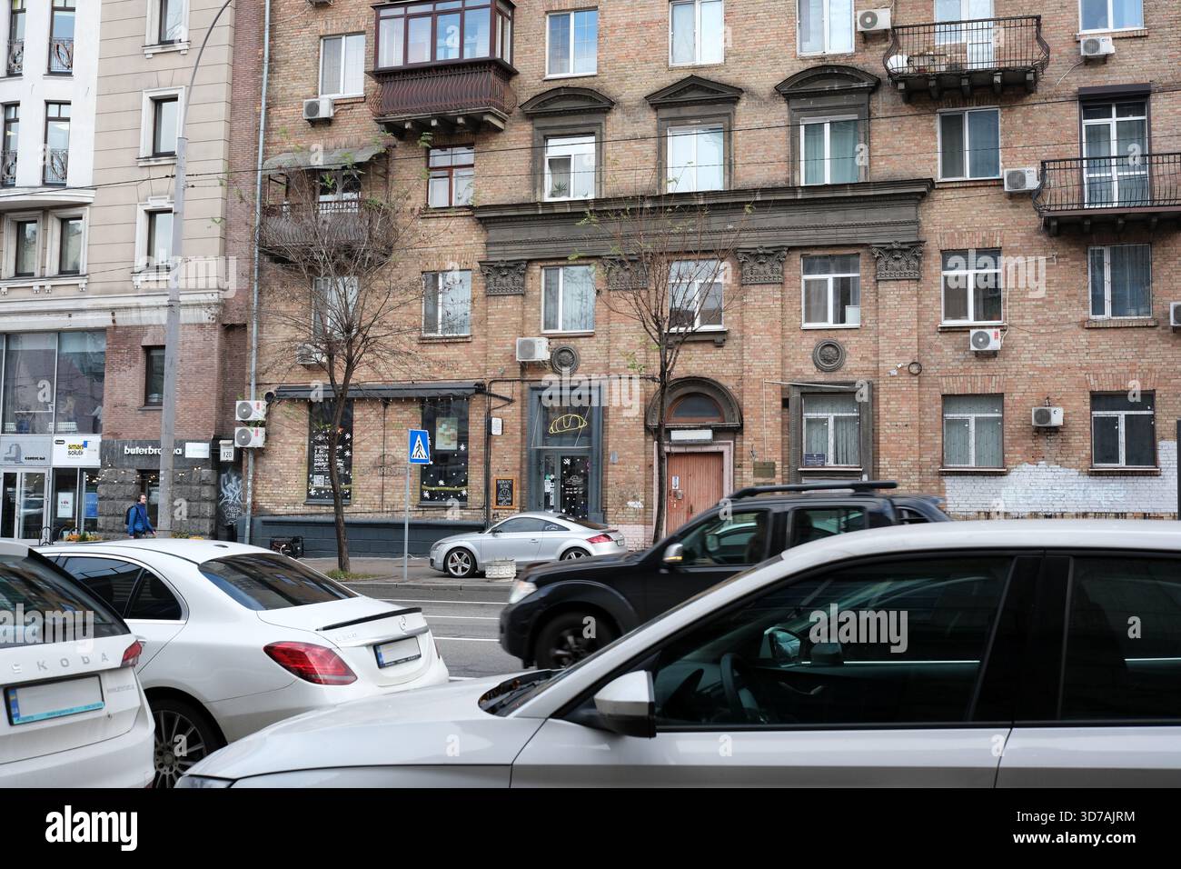 Le auto si spostano attraverso una vivace strada cittadina, mescolando vita moderna e architettura. 24 novembre 2025 Kiev, Ucraina Foto Stock