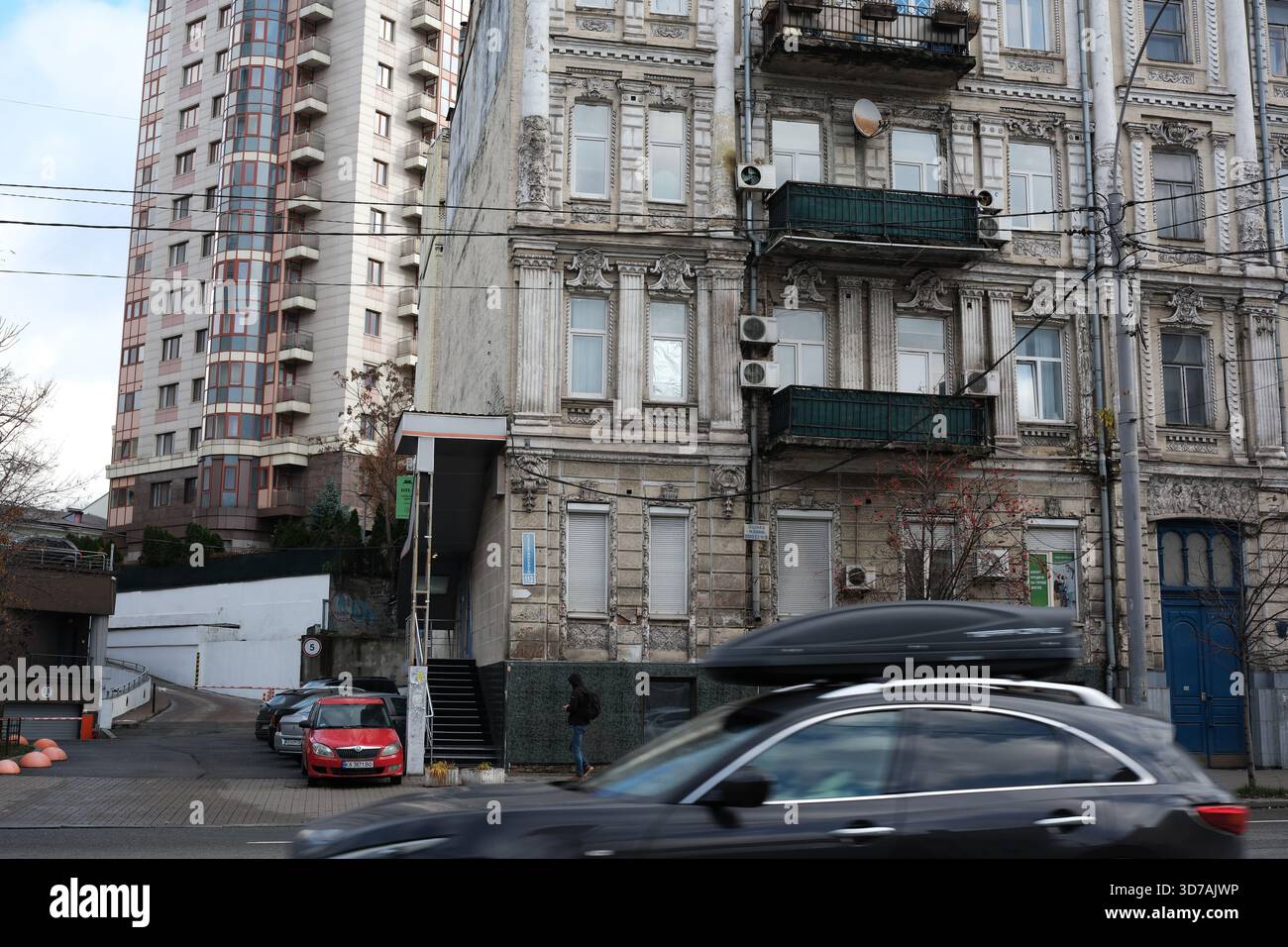 Le auto passano accanto a un vecchio edificio caratterizzato da elementi classici e da un ambiente moderno. 24 novembre 2025 Kiev, Ucraina Foto Stock