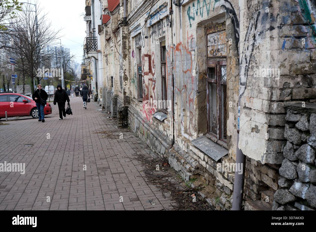 La gente passa davanti a un edificio logoro adornato di graffiti in una strada tranquilla. 24 novembre 2025, Kiev, Ucraina, Shevchenko Boulevard Foto Stock