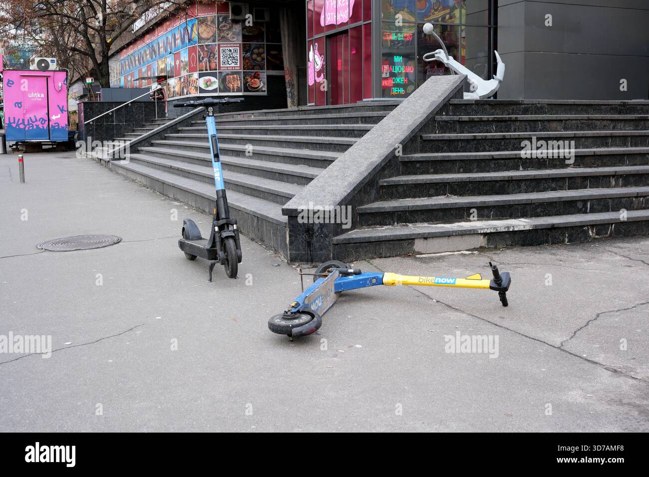 Due scooter elettrici si trovano sui gradini di una vivace area gastronomica della città. 24 novembre 2025 Kiev, Ucraina, Galitska Square. Foto Stock