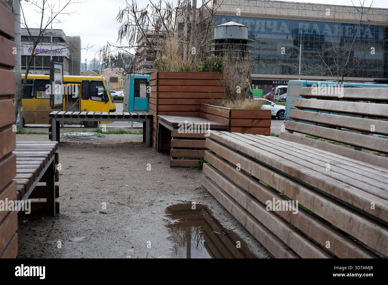 Le panche in legno fiancheggiano un piccolo parco urbano, caratterizzato da pozzanghere provenienti dalla recente pioggia. 24 novembre 2025 Kiev, Ucraina, Galitska Square. Foto Stock