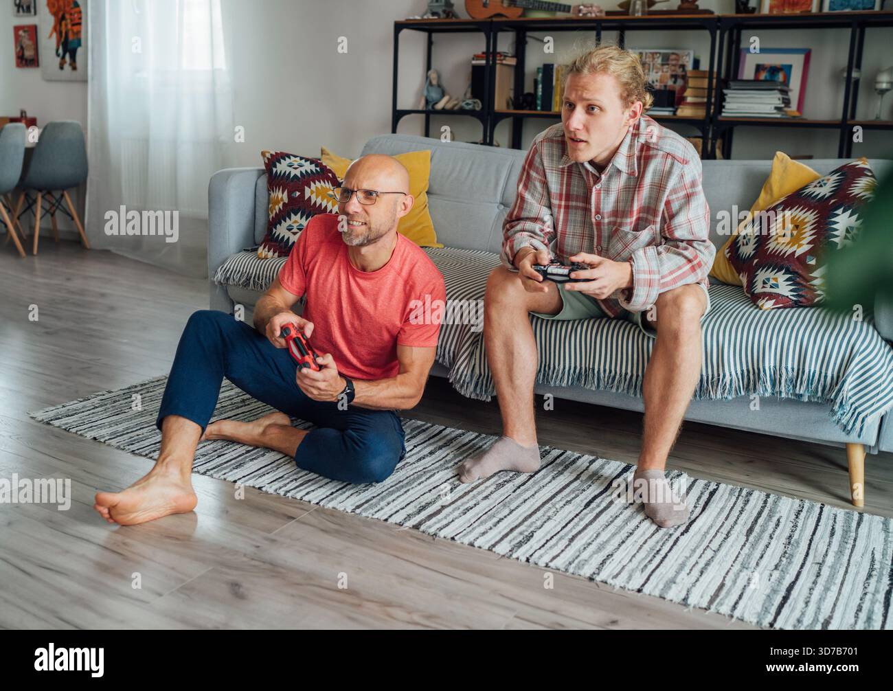 Padre e figlio si divertono con una sessione di gioco emotiva sul comodo divano del salotto che condivide l'espressione giocosa attraverso l'intrattenimento elettronico interattivo Foto Stock