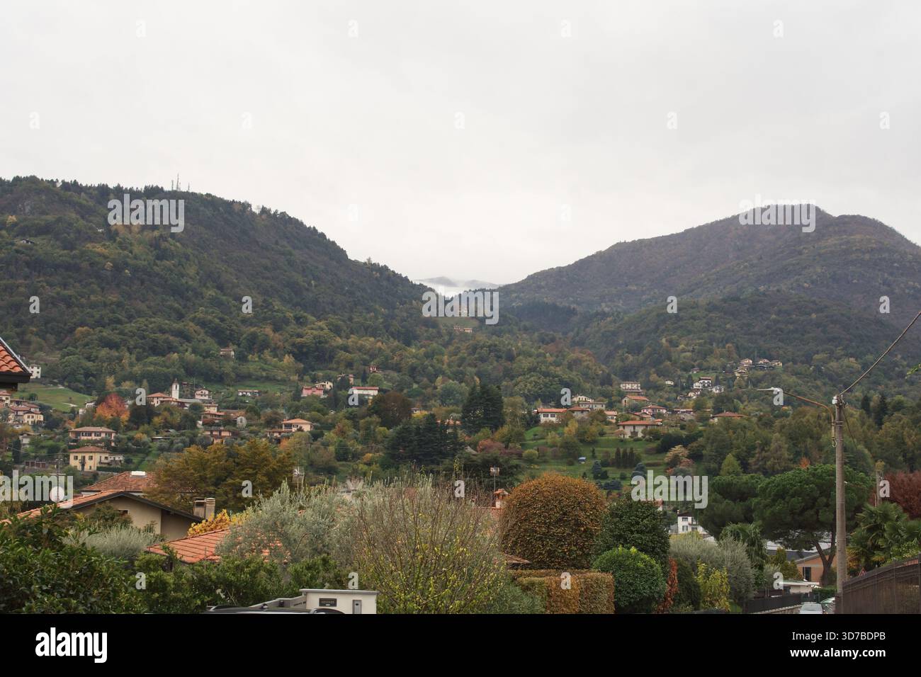 Un paesaggio ad ampio angolo di una costa ripida, rocciosa e densamente boscosa che incontra le calme acque grigie di un grande lago di Como in Italia Foto Stock