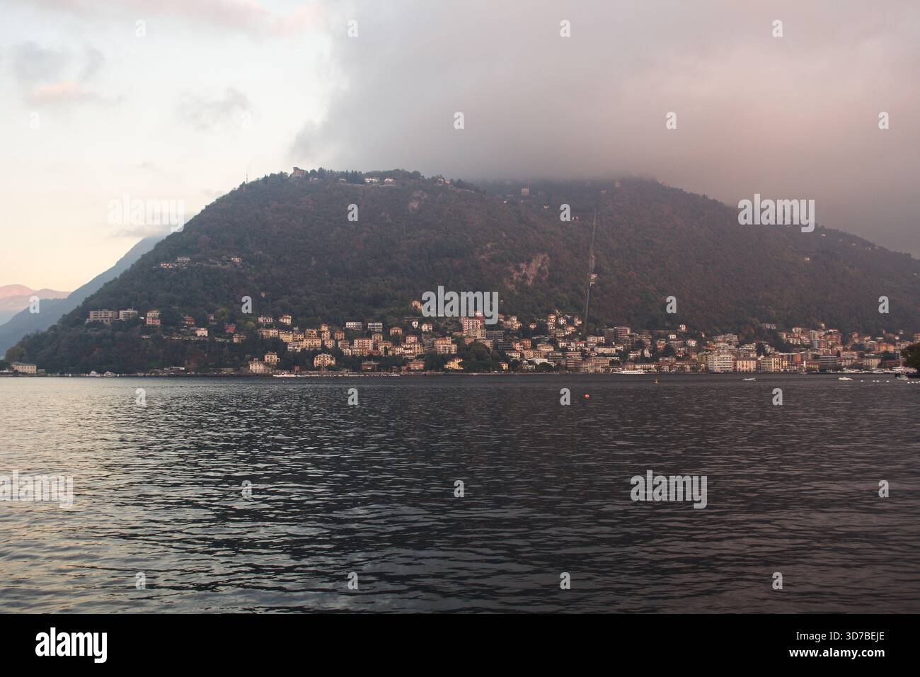 Un paesaggio ad ampio angolo di una costa ripida, rocciosa e densamente boscosa che incontra le calme acque grigie di un grande lago di Como in Italia Foto Stock