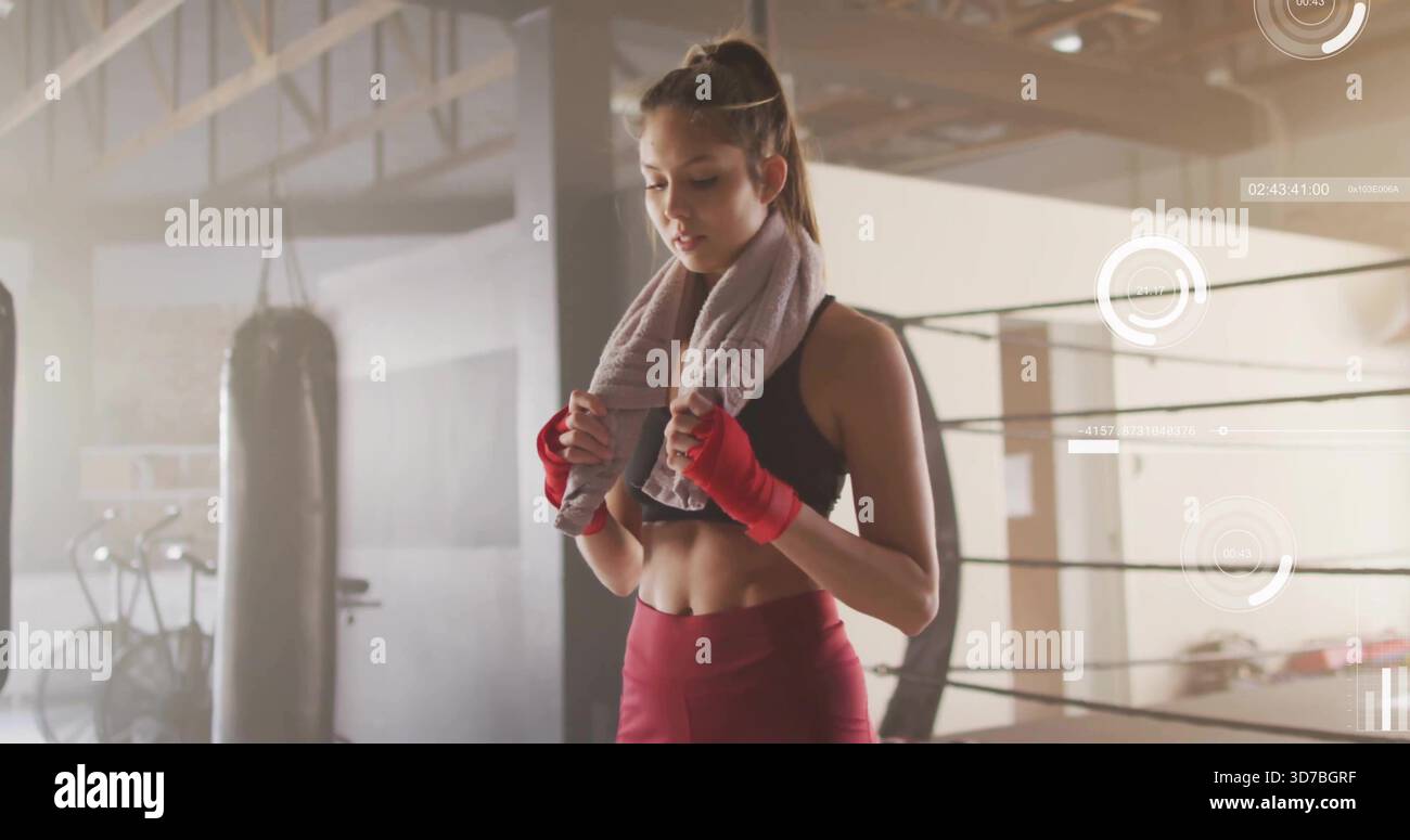 Tenendo in mano un asciugamano grigio, un pugile con reggiseno nero, leggings color marrone che si fermano con un sacchetto di punzonatura, corde ad anello Foto Stock