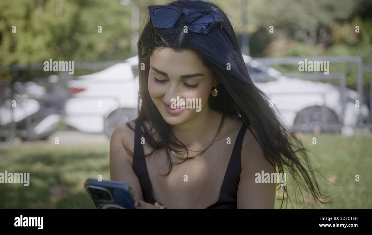 Donna che si gode una giornata di sole all'aperto con smartphone Foto Stock