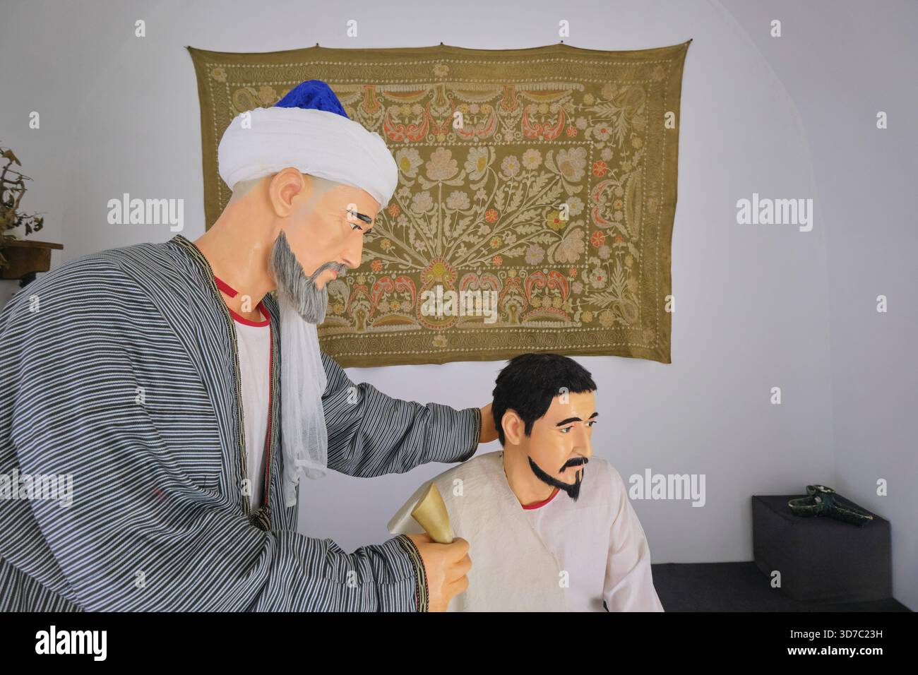 Diorama ricreativo di un medico dell'era della via della seta che esamina un paziente. Al museo medico di Shergazi Khan Madrasa. A Itchan Kala, Khiva, Uzbekistan. Foto Stock