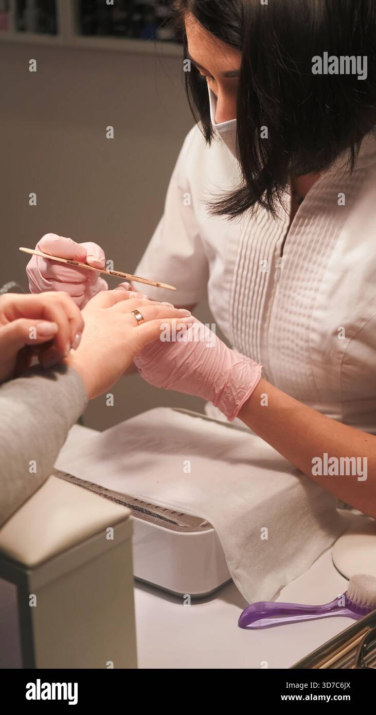 Manicure professionale. Lima per unghie. Una donna di bellezza indossa i guanti utilizzando una smeriglio su un trattamento cosmetico di routine per la cura delle unghie acriliche. Foto Stock