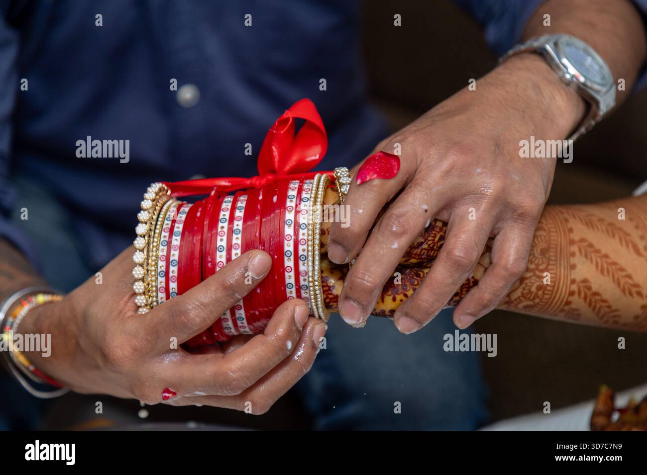 Uno scatto ravvicinato cattura le mani della sposa adornate con henné e le mani dello sposo che posizionano i braccialetti Foto Stock