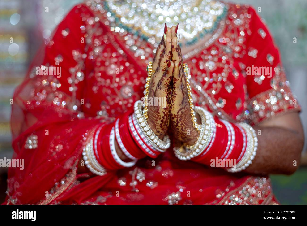 Le mani della sposa sono strette in preghiera, mostrando intricati disegni all'henné e vibranti bracciali rossi, simboleggiando un nuovo inizio Foto Stock