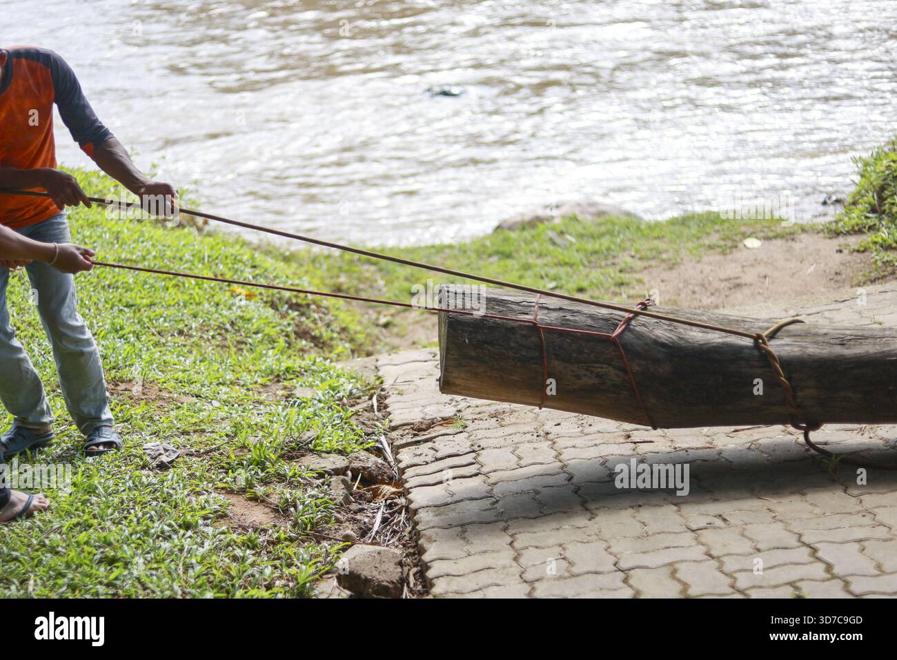 Due uomini che mostrano il lavoro di squadra e lo sforzo, tirando un grosso tronco con la corda dalla riva del fiume. mostra di duro lavoro, forza e cooperazione all'aperto naturale Foto Stock