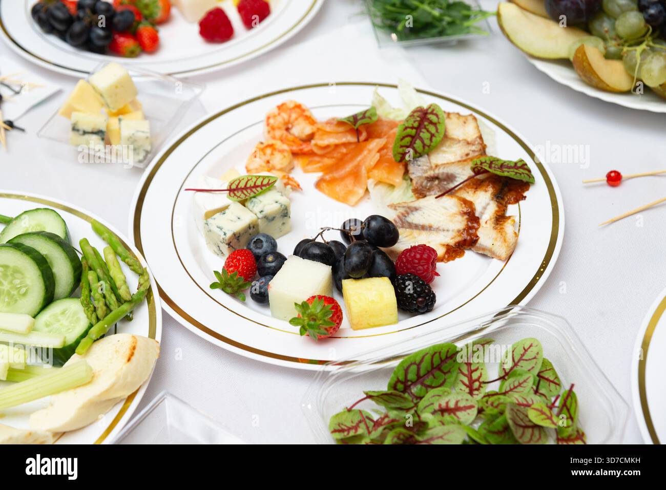 Un piatto ben organizzato che presenta un assortimento di formaggi, frutta fresca e verdi frondosi su una tovaglia bianca. perfetto per riunioni eleganti Foto Stock