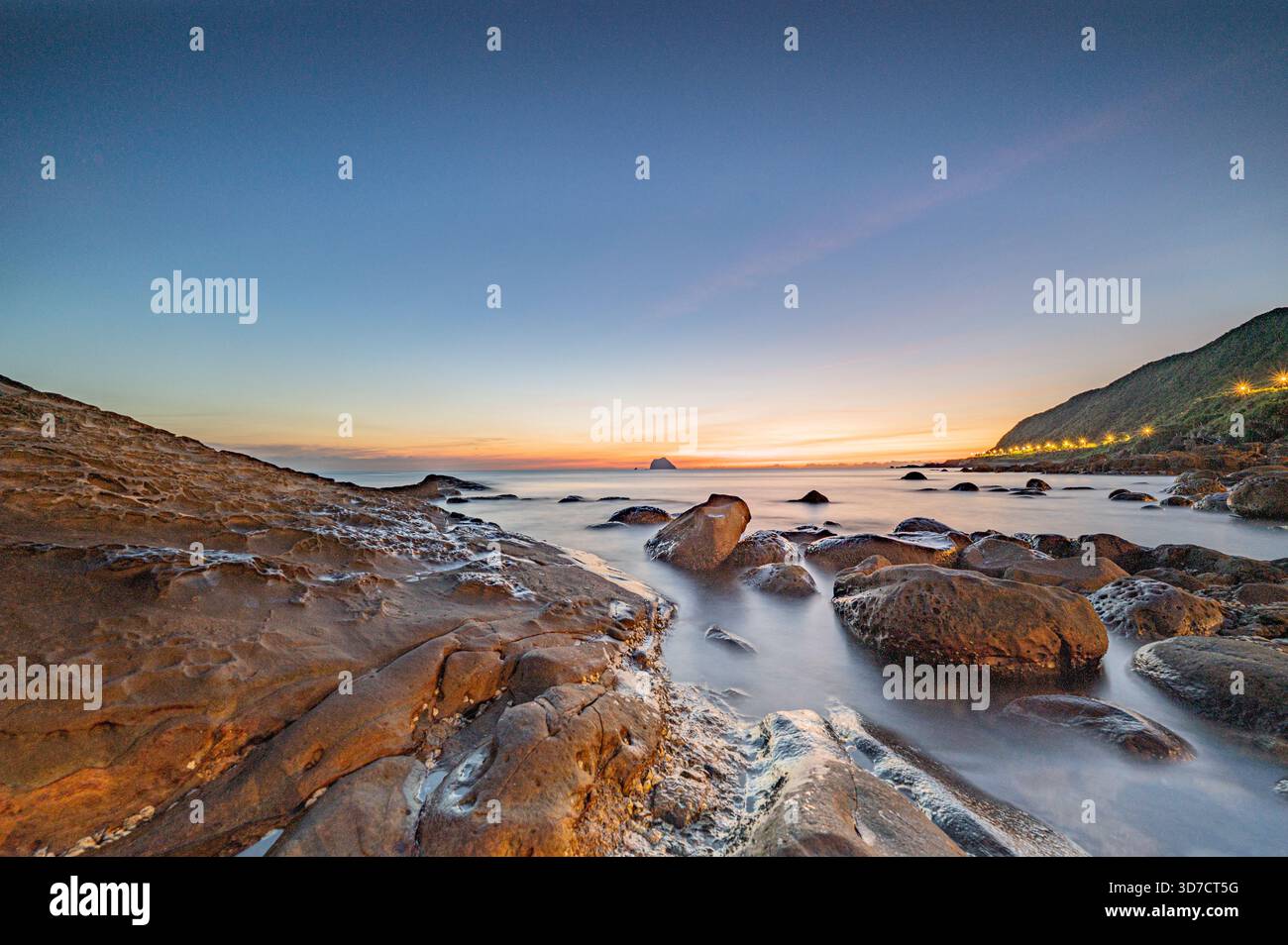Keelung Waimushan God Table, Taiwan. Il crepuscolo bacia la costa rocciosa mentre le onde nebbiose e le luci dorate tracciano un tranquillo percorso verso l'orizzonte lontano. Foto Stock