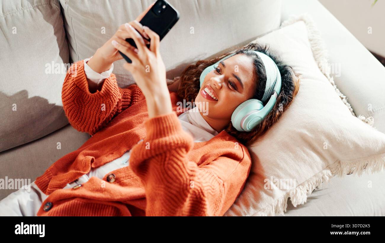 Cuffie, relax e donna con il telefono sul divano, ricerca nella libreria musicale e ascolto di podcast. Tecnologia audio, Above e persona con app radio per Foto Stock