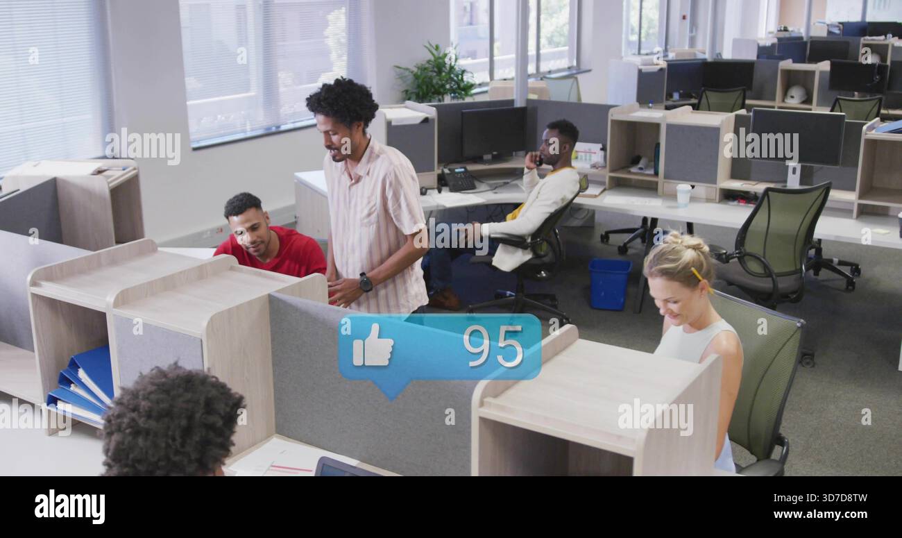 Uomo in piedi parlante a maniche corte appoggiato al cubicolo in un ufficio aperto, con sovrapposizione sociale 95 Foto Stock