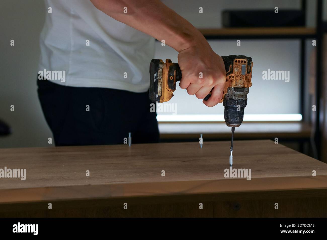 Lavoratore che assembla mobili forando le viti nel legno, visto lateralmente in ambienti interni Foto Stock